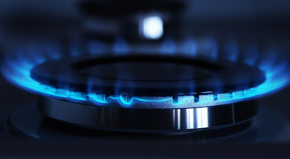 Eine blaue Gasflamme brennt auf einem Herd. Die Aufnahme zeigt den Brenner aus nächster Nähe.
