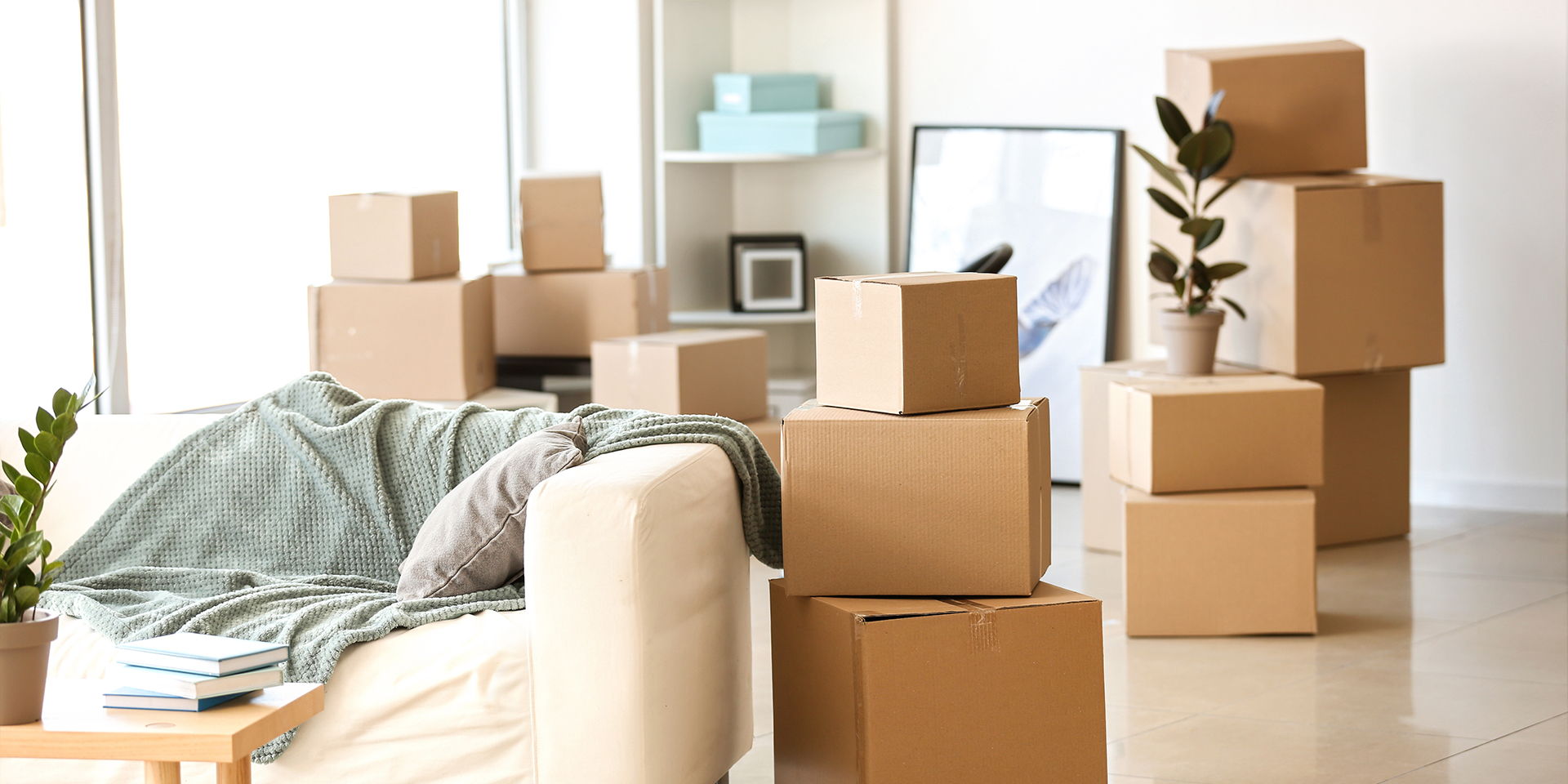 Ein Wohnzimmer mit Umzugskartons, die gestapelt im Raum stehen. Möbel und Dekoration sind teilweise bereits verpackt oder vorbereitet.