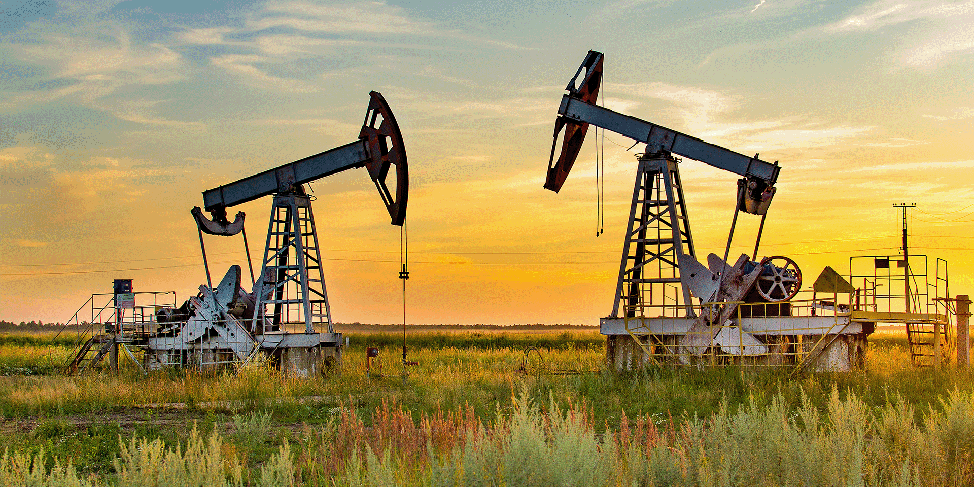 Zwei Förderpumpen stehen auf einem Feld bei Sonnenuntergang. Die Szene zeigt eine industrielle Anlage in ländlicher Umgebung.