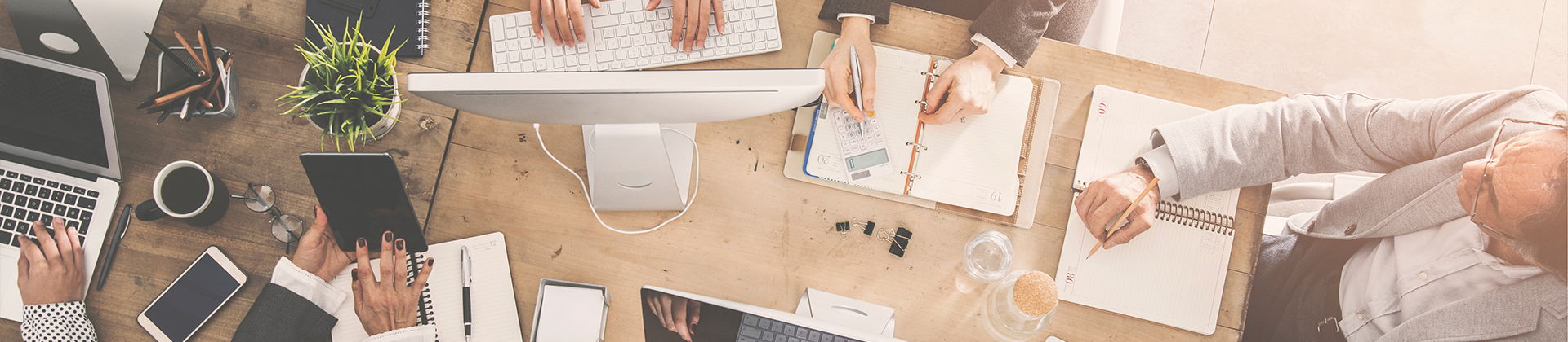 Mehrere Personen arbeiten gemeinsam an einem Tisch mit Computern, Notizen und Tablets. Die Szene zeigt eine Teamarbeit aus der Vogelperspektive.